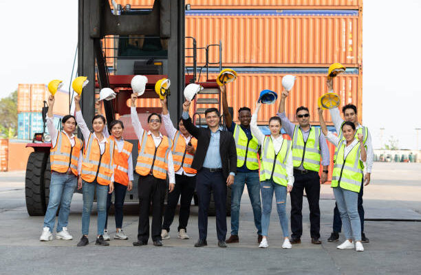 team-2 portrait factory workers or engineers team holding helmet and raise hand up for success in containers warehouse storage